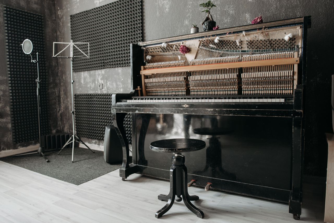 who-we-are An open vintage upright piano in a soundproof music studio with recording equipment.